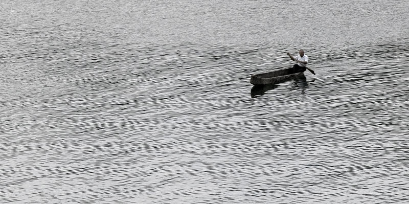 an old man rows a small canoe acorss a lake